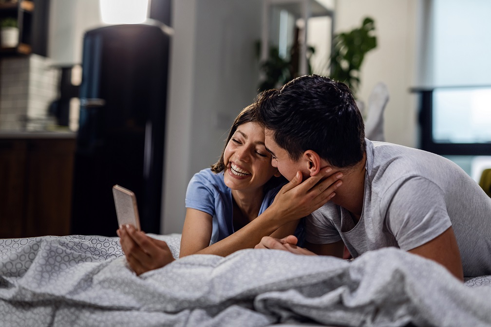 Happy couple in love taking selfie with cell phone while lying on the bed.